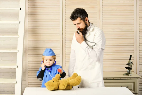 Ветеринар и маленький ассистент осматривают плюшевого мишку. Отец и ребенок — стоковое фото