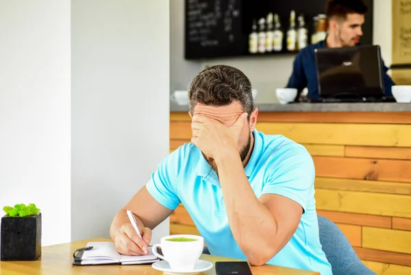 Człowieku rozczarowany rozpaczliwe twarzy siedzieć kawiarnia z kubkiem kawy i Notatnik. Ból głowy i stres. Termin najbliższych inspiracja potrzebujesz pomysłów Szukaj. Kryzys w kreatywności i inspiracji. Człowiek cierpi ból głowy — Zdjęcie stockowe