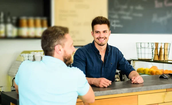 Man ask for coffee at bar counter. Barista handsome stylish hipster communicate with client visitor. Service staff qualification. Barista at bar of modern cafe ready to serve coffee for client