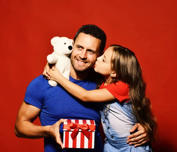 Daughter kisses her dad holding teddy bear.