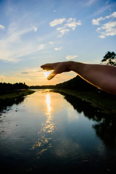 Złapać sunbeam ostatnio. Mężczyzna ręka wskazuje na słońce w błękitne niebo wieczorem czas podziwiać krajobraz. Rzeka słońca odbicie. Uchwycić moment, aby podziwiać zachód Słońca Natura piękna. Podziwiać zachód słońca nad rzeką powierzchni — Zdjęcie stockowe