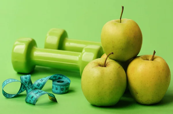 Tape measure in cyan color near barbells and juicy apples