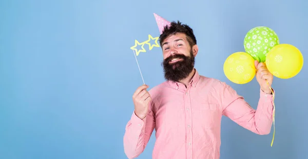 Hipster in sternförmiger Brille feiert Geburtstag. Parteizuschreibungen. Mann mit Partyhut und Luftballons feiert. Mann mit Bart im glücklichen Gesicht hält Luftballons, hellblauer Hintergrund — Stockfoto