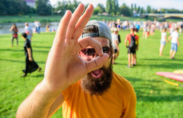 Фестиваль посещений хипстеров. Мужчина веселое лицо смотрит через хорошо жест. Мужчина бородатый на фоне толпы на берегу реки. Забронируйте билеты на летний фестиваль заранее. Будьте уверены в летнем отпуске
