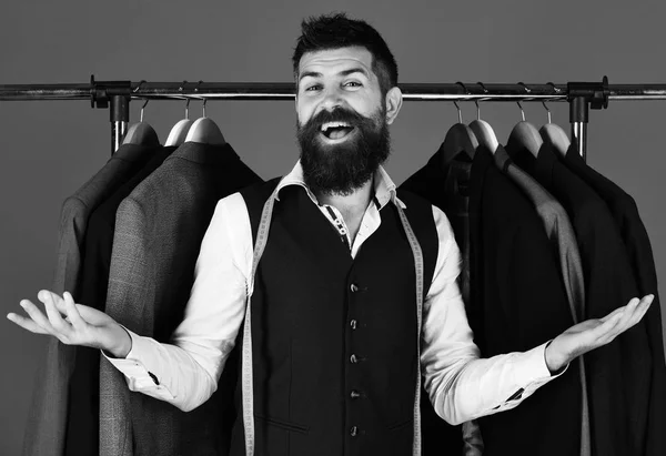 Man with beard by clothes rack. Tailor with excited face