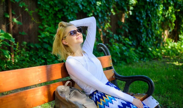 Блондинка в солнечных очках мечтает об отпуске, отдыхает в парке. Девушка сидеть скамейка отдыха в тени, зеленый фон природы. Леди нужно расслабиться и отдохнуть. Отпуск мечты — стоковое фото