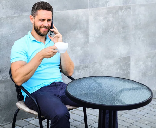 Descanso de café trae bienestar físico y mental. Hombre sentarse terraza y beber cappuccino hablar teléfono gris fondo de la pared. Es hora de relajarse. Breve descanso café proporciona a los empleados con formas rápidas de relajarse — Foto de Stock