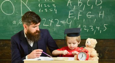 Matematik ders kavramı. Hevesli çocuk öğretmen ile eğitim. Baba oğul matematik öğretiyor. Öğretmen formal giyim ve öğrenci sınıfta kolej, kara tahta arka plan