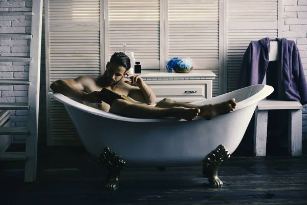 Sexual- und Entspannungskonzept: Macho sitzt in Badewanne und liest Buch — Stockfoto