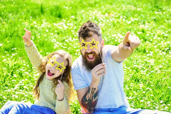 Concept de rock star. Père et fille sont assis sur l'herbe à la prairie, fond vert. La famille passe ses loisirs à l'extérieur. Enfant et papa posant avec des lunettes en forme d'étoile attribut photomaton au pré — Photo