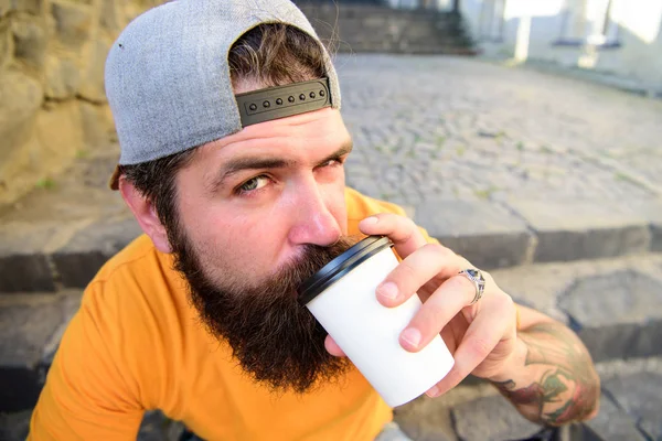 Man bearded hipster enjoy drink paper cup urban background. Hipster drink coffee to go while sit stairs outdoors. Urban food culture concept. Tasty sip concept. Tasty coffee tea in paper cup close up — Stock Photo, Image