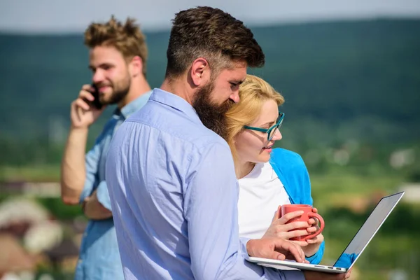 Coffee break concept. Colleagues with laptop work outdoor sunny day, nature background. Business partners meeting non formal atmosphere. Colleagues pay attention screen laptop while man talking phone