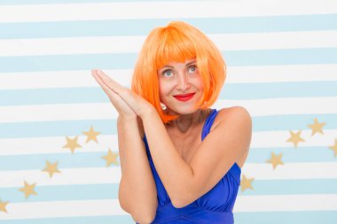 Aktris yetenekleri konsepti. Sevimli duygusal ifade üzerinde çalışan bir kadın. Kadın oyuncu performans çalışıyor. Stüdyonun çizgili arka planında poz veren kız. Kırmızı ya da mavi elbiseli kızıl peruk