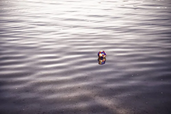 Bola de brinquedo colorido, atributo de jogo de futebol refletindo em água ondulada — Fotografia de Stock