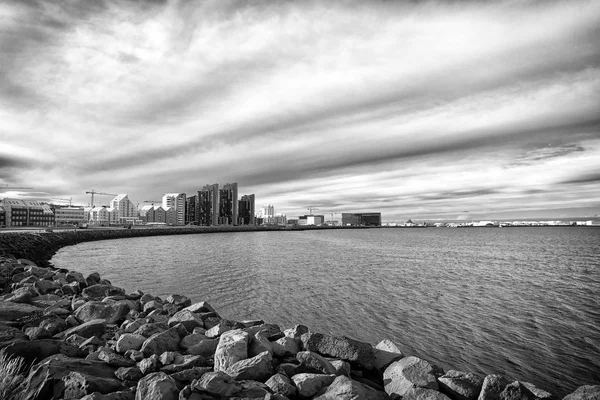 Paisaje marino con costa de piedra en reykjavik, iceland. Edificio de la ciudad al lado del mar. Skyline en el cielo nublado. Arquitectura y construcción. Wanderlust o viajar y aventura —  Fotos de Stock