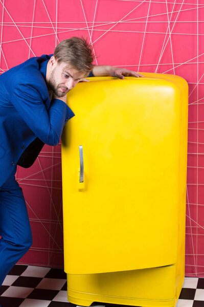 Мужчина формальный элегантный костюм стоять рядом с ретро винтажный желтый холодильник. Винтажные бытовые приборы. Голодные холостяки думают, что едят возле холодильника. Яркий холодильник бытовой техники. Голод и аппетит
