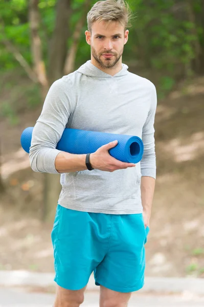 Alongamento músculos pilates praticar. Sportsman carrega tapete de ioga para exercícios ao ar livre. Conceito de ioga exterior. Homem atleta rosto calmo carrega tapete para esticar o fundo da natureza. Atleta treinador desportista — Fotografia de Stock