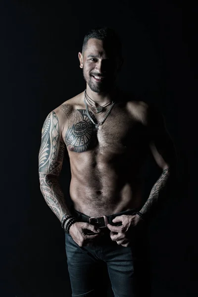 Bearded man smile shirtless with fit torso. Man with tattoo design on skin. Fashion model buckle leather belt in jeans. Sportsman with six pack and ab. Fitness with sport and bodycare, vintage filter — Stock Photo, Image