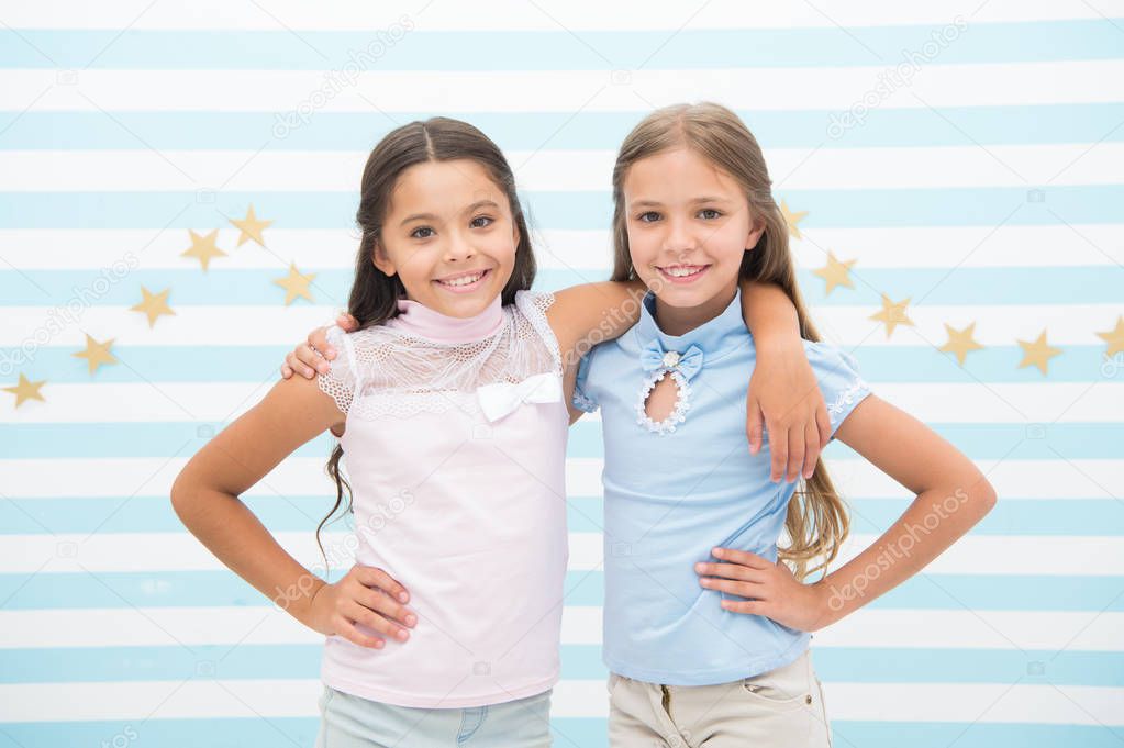 Happy childhood concept. Kids schoolgirls preteens happy together. Friendship from childhood. Girls smiling happy faces hug each other while stand striped background. Girls children best friends hugs
