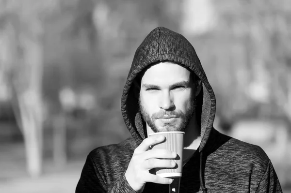 Bearded man with takeaway drink in sunny park. Macho in hood hold disposable coffee cup. Coffee or tea mood. Drink and food outdoor. Morning tea for breakfast