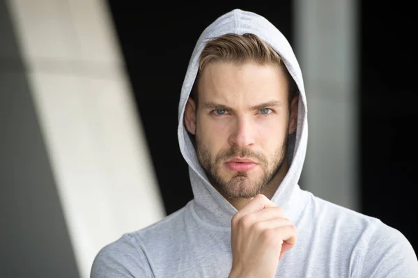 Focused future achievement. Guy bearded attractive casual clothes hooded. Man with bristle concentrated face urban background defocused. Man unshaven guy looks handsome hooded. Concentrated on goal