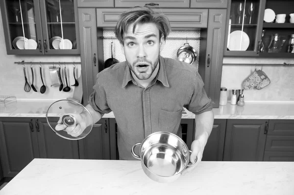 Guy with surprised face hold open saucepan, lid in kitchen