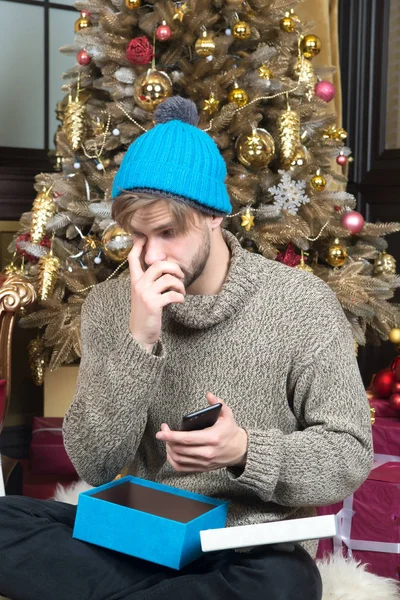 Man open present box with smartphone at Christmas tree