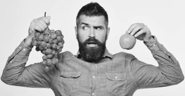 Sakallı adam bir demet yeşil üzüm ve elma tutuyor.