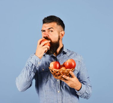 Sakallı adam elinde meyve dolu hasır kasesi tutuyor.