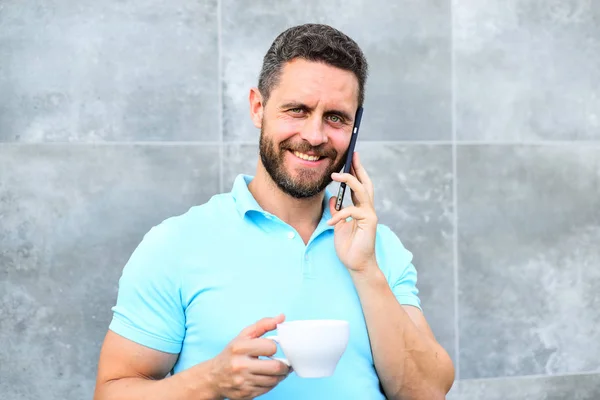 Incluso si usted bebe café sobre la marcha cada sorbo es poco descanso en su día y poco momento de autocuidado. Hombre beber cappuccino hablar teléfono gris fondo de la pared. Razones por las que los empresarios beben café — Foto de Stock