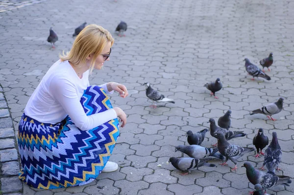 Tauben warten auf dem Stadtplatz auf Leckereien. Großzügigkeit teilen. Mädchen blonde Frau entspannen Stadtplatz und Tauben füttern. Touristinnen oder Bürger werfen Krümel für Tauben. Mädchen füttert Taubenvögel — Stockfoto
