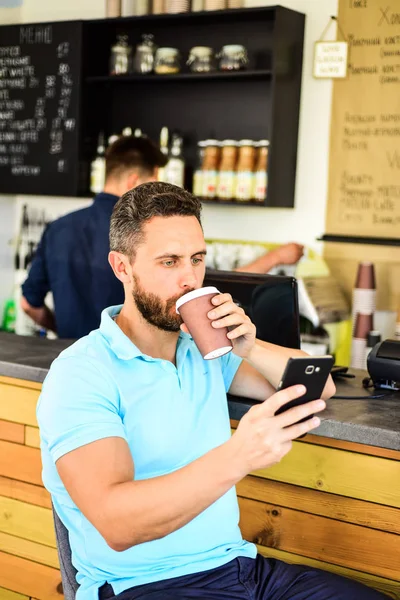 Confident entrepreneur choose drink in paper cup to go while communicate mobile. Man surfing internet and drink coffee cafe bar background. Man solving problems phone have coffee. Always in touch