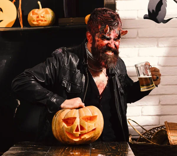 Man wearing scary makeup holds mug of beer on Halloween