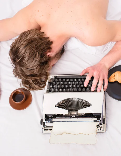 Author tousled hair fall asleep while write chapter top view. Man with typewriter coffee lay bed. Man sleepy lay bedclothes while work. Writer used old fashioned typewriter. Workaholic fall asleep.