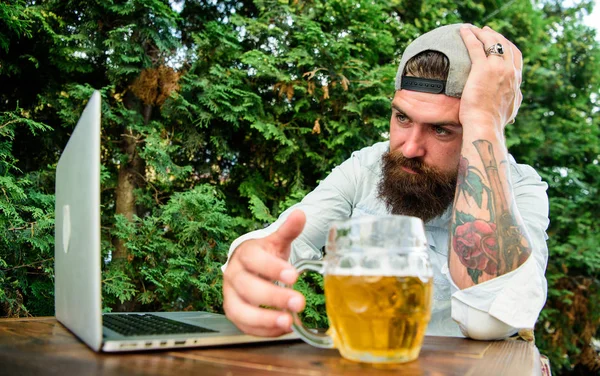 Brutal man leisure with beer and sport game. Fan watch stream online while sit terrace outdoors drink beer. Football fan bearded hipster watch game on laptop screen. Disappointed with game result