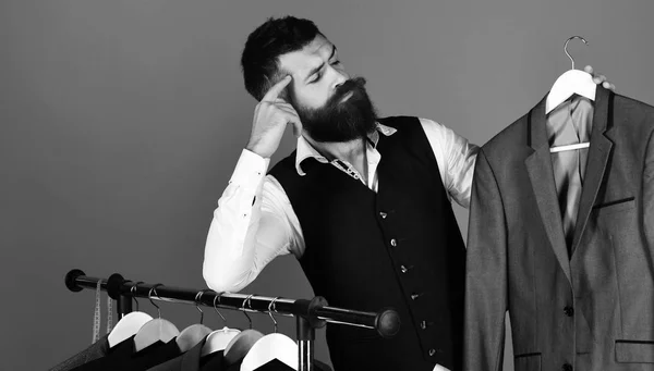 Man with beard by clothes rack. Designer looks at work