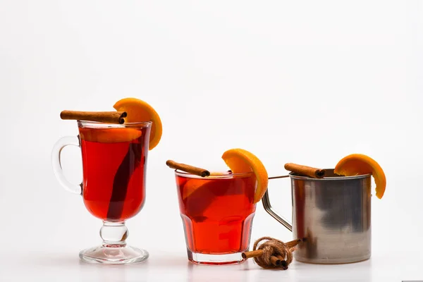 Drink or hot beverage with orange and cinnamon in glasses and metal mug. Bar serving concept. Glasses and mug with mulled wine with orange and cinnamon on white background, close up — Stock Photo, Image