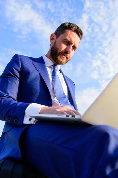 Businessman surfing internet or reply emails while sit with laptop outdoors. Sales manager works on internet marketing blue sky background. Increase online sales tips. Tips create amazing cold emails