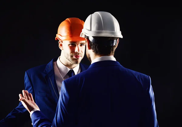 Engineers isolated on black background. Technical architect talks to project manager with unsatisfied face. Coworkers in formal suits and building helmets. Construction management concept