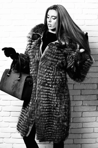 Młoda modne sexy dość bogaty kobieta z piękne długie blond włosy w pasie płaszcz szary futro w czarne rękawiczki pokazując niebieski skórzana torba z węża odcisk na cegły ściany studio tło — Zdjęcie stockowe