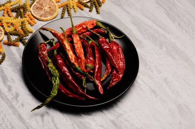 Kırmızı biber ve siyah seramik tabak içinde makarna ve malzemeler.