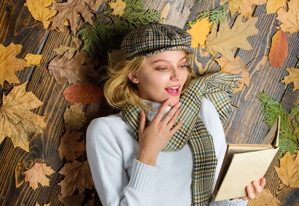 Fall and autumn season. She likes detective genre. Girl blonde lay wooden background with leaves top view. Woman lady in checkered hat and scarf read book. Girl in vintage outfit enjoy literature