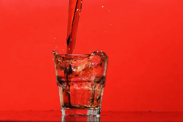 Spruzzi d'acqua in vetro per whisky su fondo rosso, copiare spazio . — Foto Stock