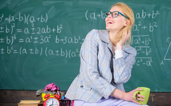 Tómate un descanso. Condiciones de trabajo para los profesores. Mujer sonriente profesor sostiene taza beber sentarse mesa aula pizarra fondo. Condiciones de trabajo que deben tener en cuenta los futuros profesores — Foto de Stock