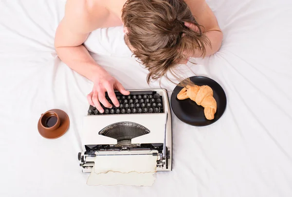 Uomo ispirato laici biancheria da letto libro di lavoro. Scrittore autore usato vecchia macchina da scrivere. Uomo con macchina da scrivere e caffè giaceva letto. Autore guy tousled capelli occupato scrivere capitolo scadenza coming top view — Foto Stock