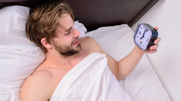 Mantenha o horário de dormir na mesma hora de dormir e acorde. Conceito de hábitos de regime de sono. Homem sonolento sonolento sem barba rosto coberto com cobertor tendo descanso. Homem unshaven lay desperta cama segurar despertador — Fotografia de Stock