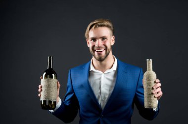 Sommelier 'de iki şişe şarap var. Profesyonel şarap arıtma konsepti. Elinde şarap şişeleri olan resmi takım elbiseli bir adam. Sommelier yakışıklı, esmer arka plandaki neşeli adam. Hangi şarabı seversin?