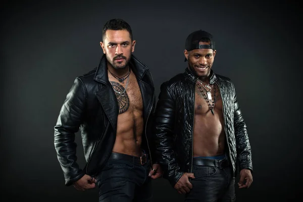 Masculinity and brutality concept. Men with sexy muscular torsos look brutally. Machos with muscular torsos look attractive in leather jackets, dark background. Men on smiling faces with bristle