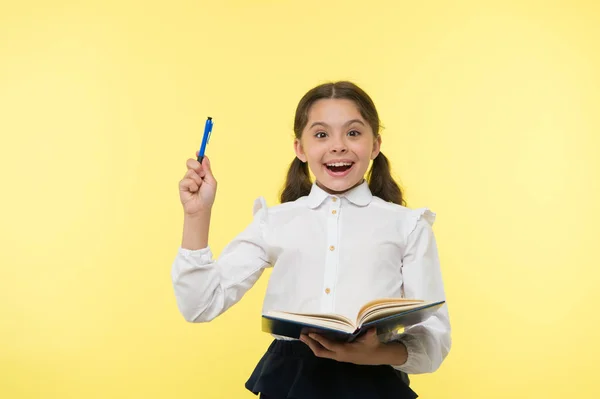 Girl cute schoolgirl in uniform hold book or textbook yellow background. Diligent pupil get knowledge from book. Child wear school uniform prepare for lesson her knowledge. Excited about knowledge — Stock Photo, Image