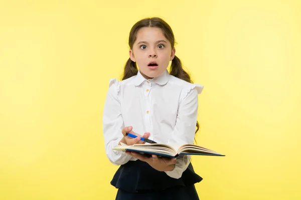 Girl cute schoolgirl in uniform hold book with information yellow background. Pupil get information from book. Child wear school uniform prepare for lesson information. Surprised about information — Stock Photo, Image